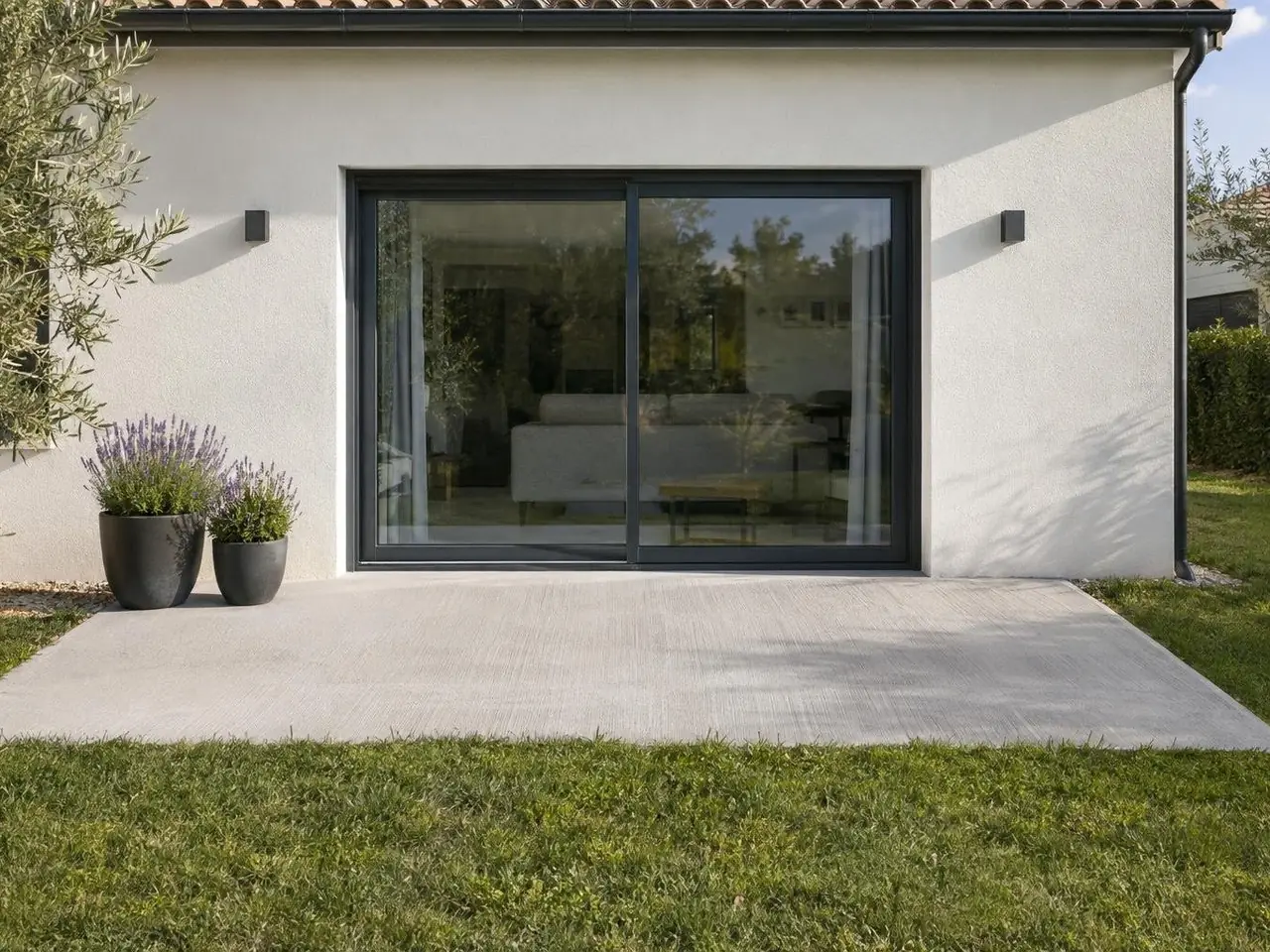 Terrasse en béton balayé gris clair devant une baie vitrée anthracite, deux pots de lavande sur un coin