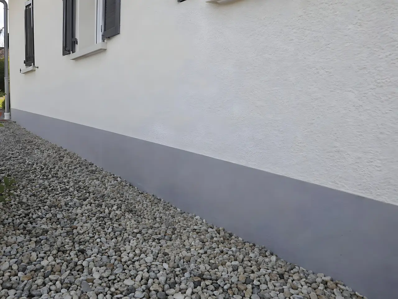 Le même soubassement refait en gris lisse et net le long de la façade blanche et des graviers