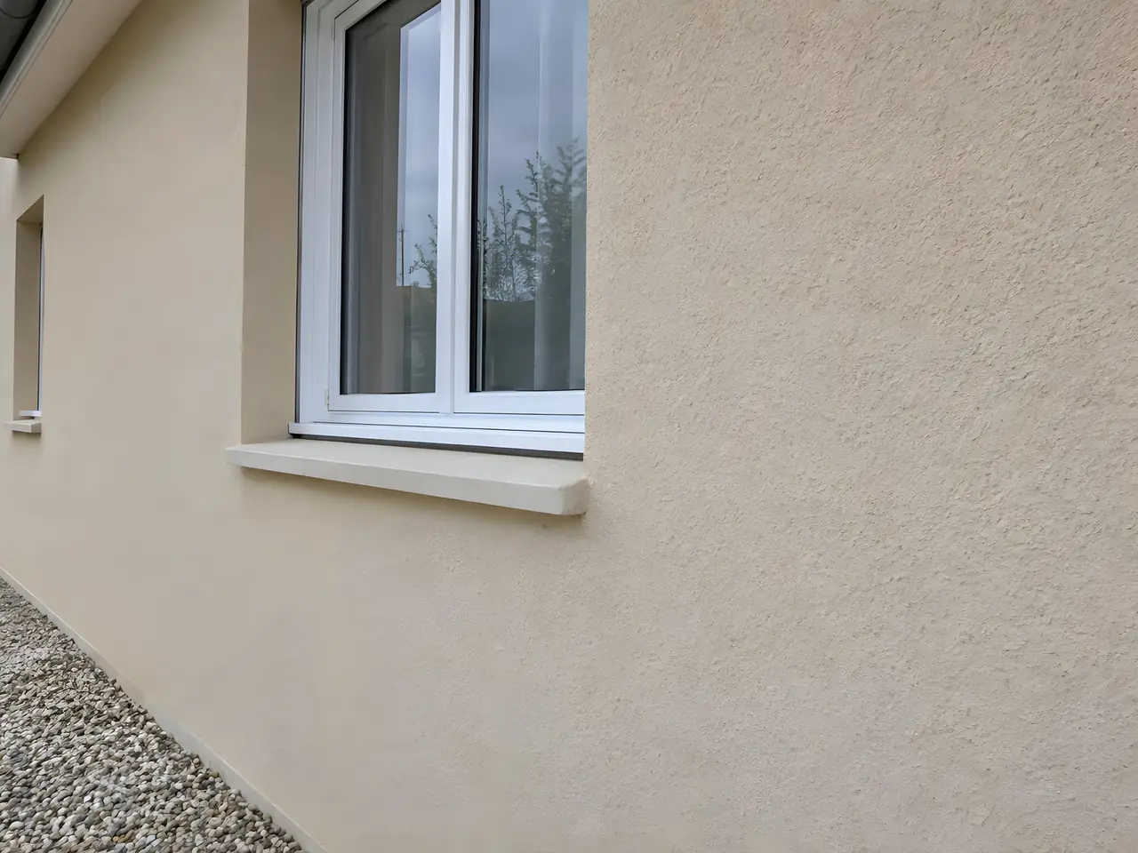 La même façade beige sous la fenêtre, fissure et éclat rebouchés, enduit uniforme sans trace