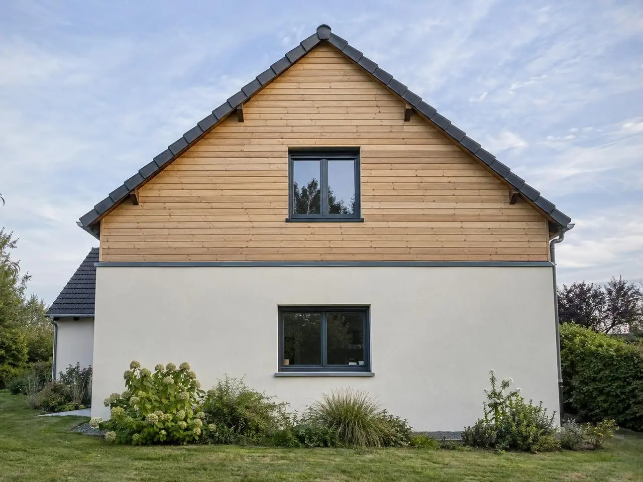 Pignon de maison au haut habillé de lames de mélèze horizontales, bas en crépi blanc cassé, toit de tuiles grises
