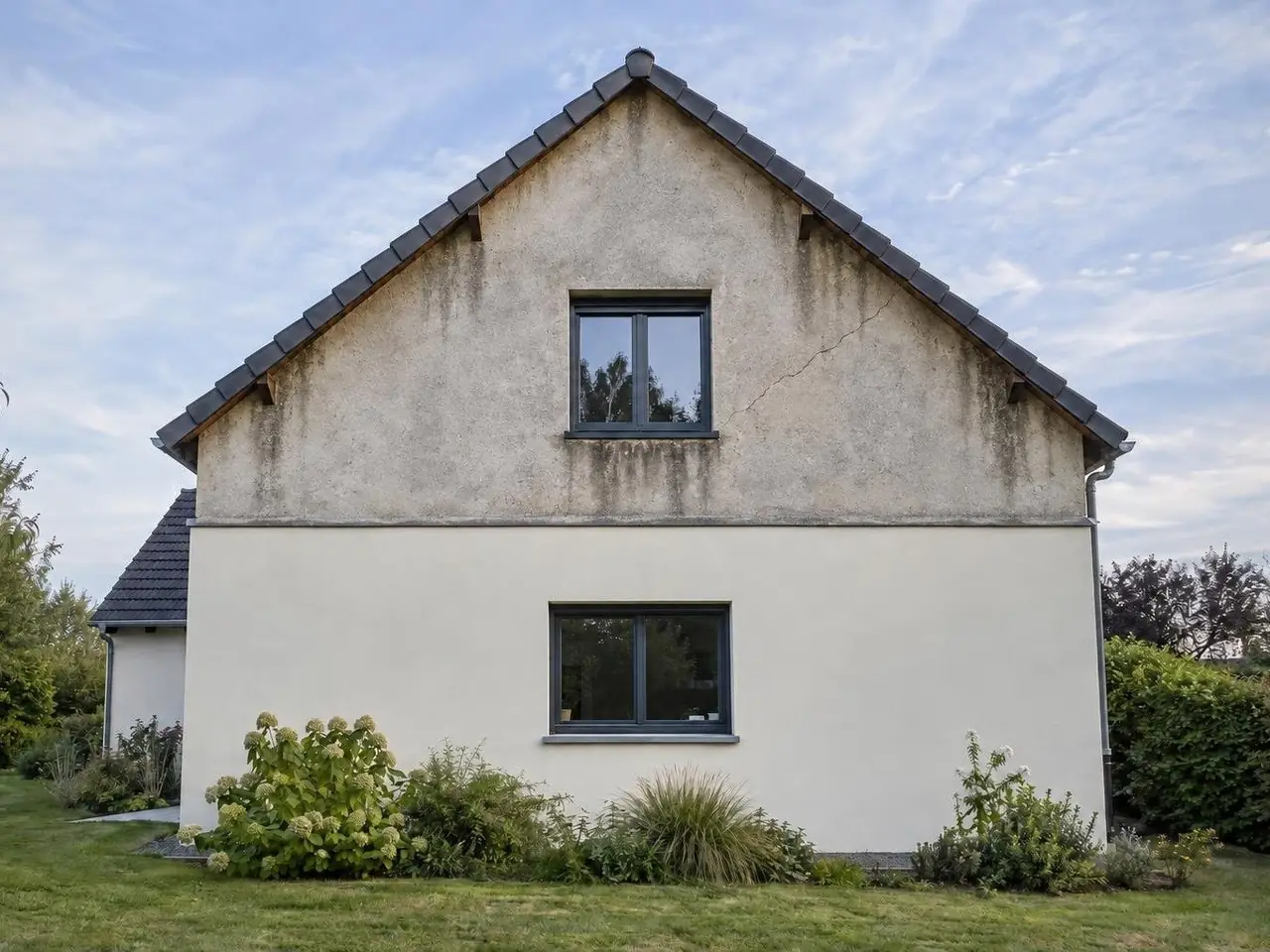 Pignon de maison au haut en vieux crépi gris taché de coulures noires et fendu en biais, bas en crépi blanc cassé