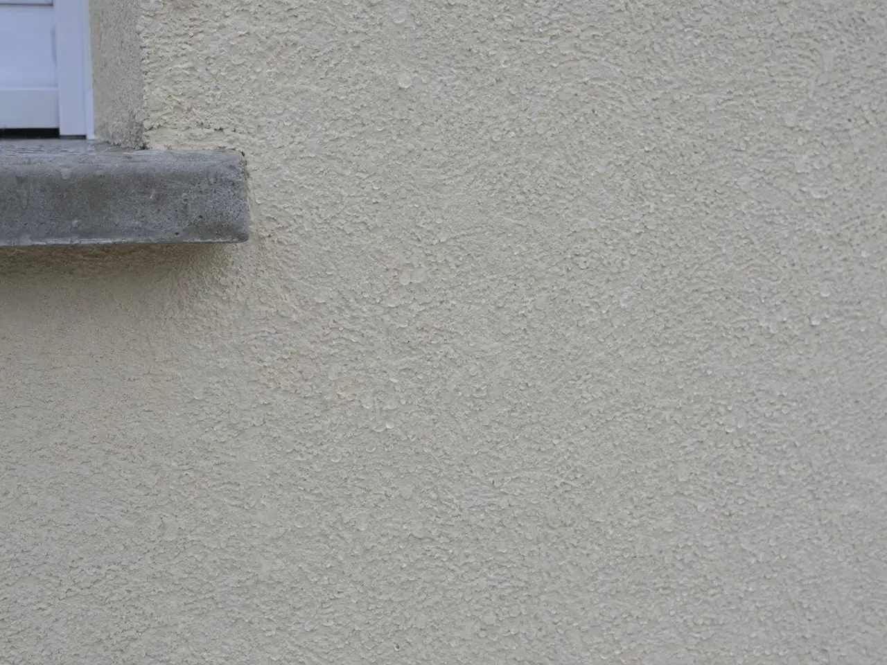 Crépi beige clair propre et de teinte égale sous l'angle d'un appui de fenêtre en béton gris, grain bien net