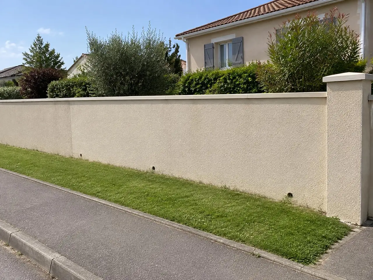 Mur de clôture remonté et enduit beige, chaperon neuf, pilier à chapeau et trous d'écoulement au pied