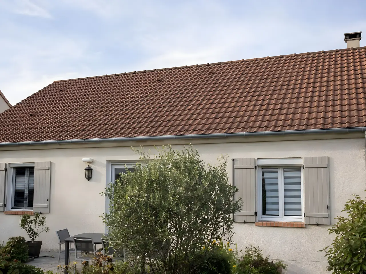 Toit en tuiles rouges d'un pavillon au crépi clair, tuiles nettes et uniformes au-dessus des volets gris