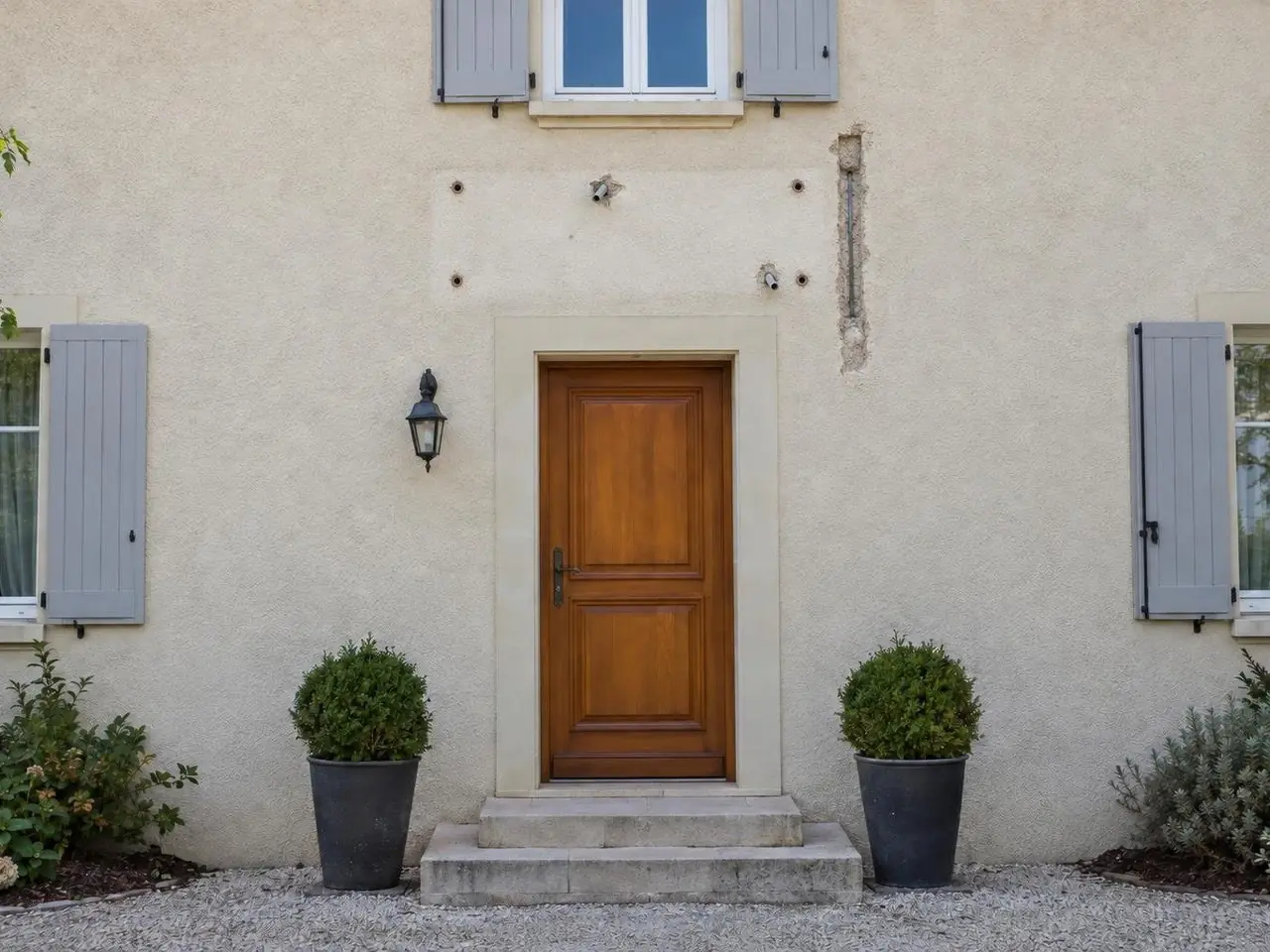Façade en crépi beige au-dessus d'une porte en bois, empreinte d'auvent démonté avec trous, chevilles et saignée ouverte