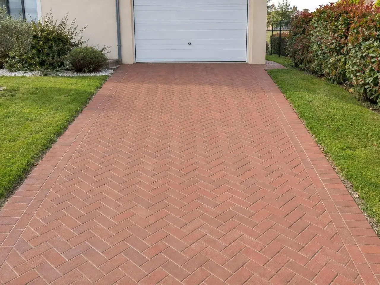 Allée de pavés ocre rouge en chevrons, couleur vive, joints nets, menant à une porte de garage blanche