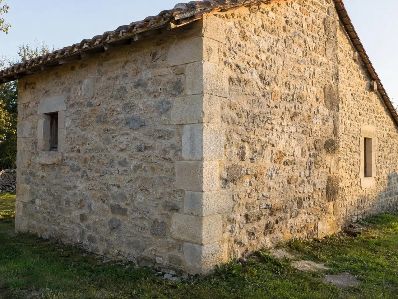 Angle d'une dépendance en pierre au toit de tuiles anciennes, pierres d'angle taillées alignées du sol au toit